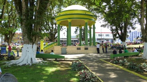 El quiosco verde y amarillo del parque central de Ciudad Quesada, rodeado de árboles, bancas y personas paseando.