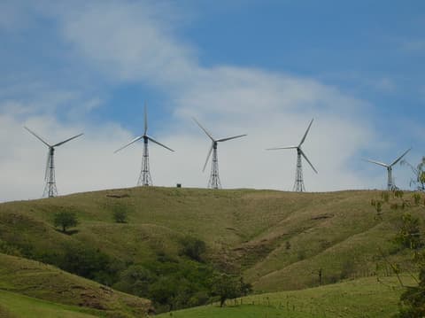 Una fila de aerogeneradores sobre lomas de potrero verdes en Tierras Morenas, cerca del lago Arenal.