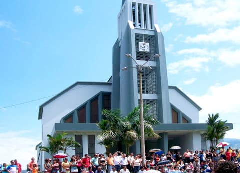 La catedral de Ciudad Quesada, un edificio moderno gris y blanco con una torre alta y un reloj, con una multitud frente a ella.