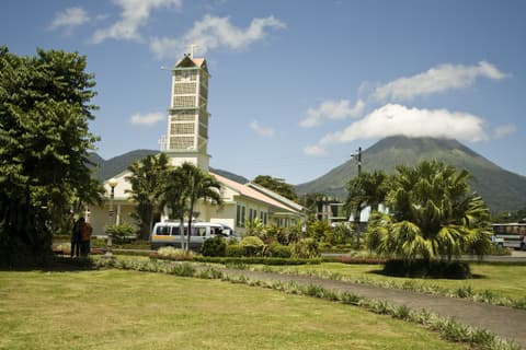 El parque central de La Fortuna con el templo católico a la izquierda y el volcán Arenal al fondo, con la cima entre nubes.