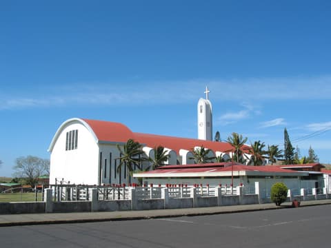 Tilarán's cathedral, a white church with a red roof, a slender tower and a cross, under a blue sky.