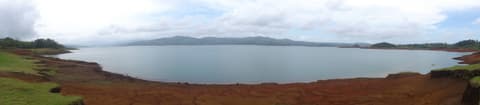 Panorámica del lago Arenal desde Nuevo Arenal, con la orilla de tierra rojiza en primer plano.